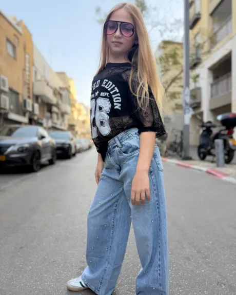 חולצת תחרה שחורה אוברסייז בצבע שחור שקוף עם הדפס לבן של 26 וג׳ינס כחול בהיר, מבט מקדימה
